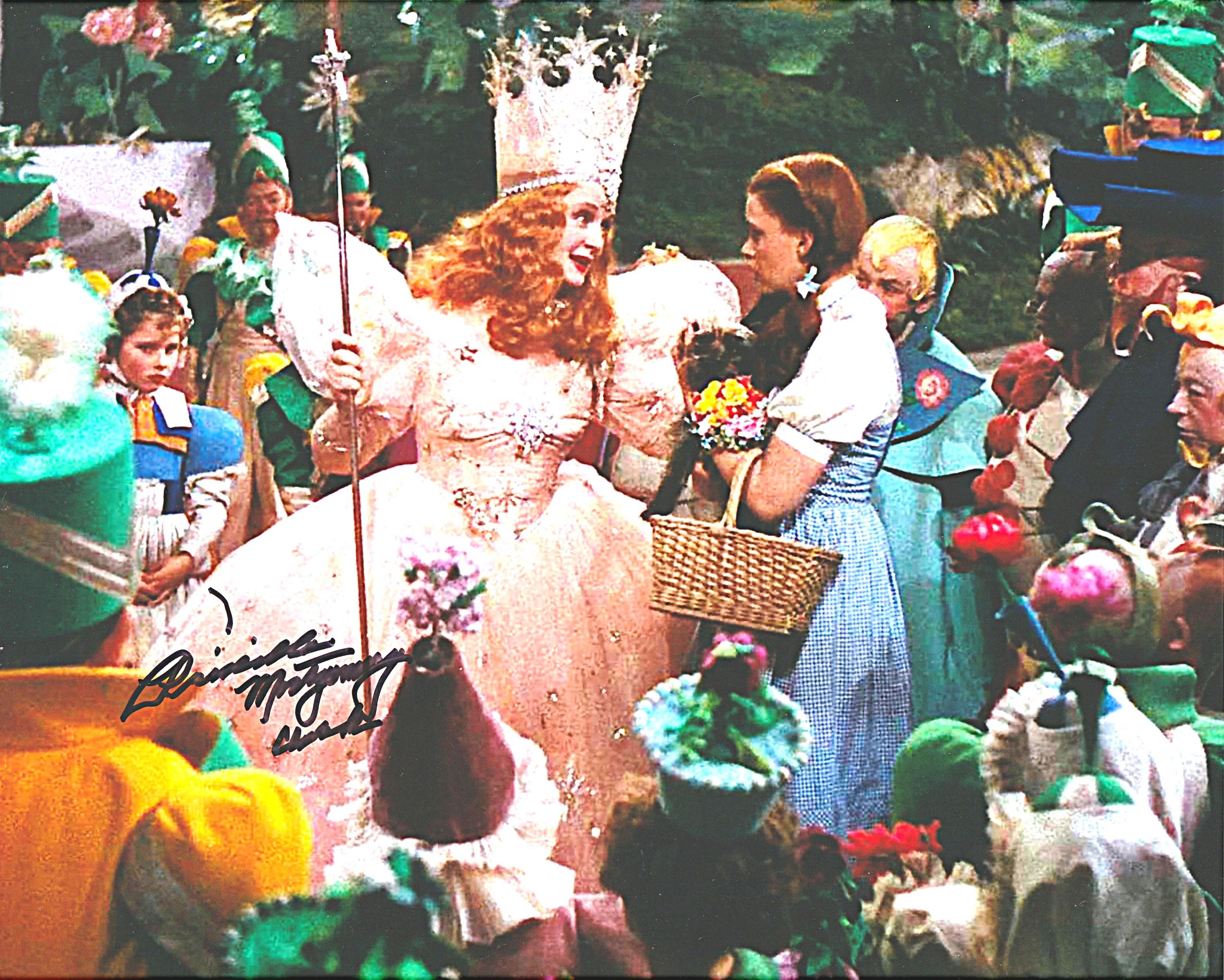 Glinda the Good Witch speaks with Dorothy as Munchkins gather around in Munchkinland; signed by child Munchkin Priscilla Montgomery Clark.